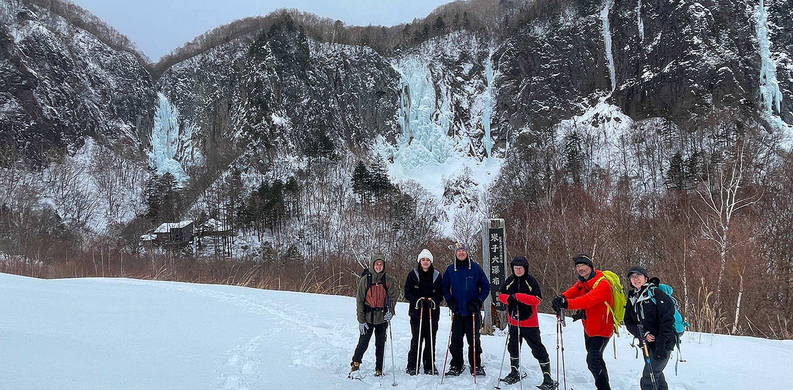 米子大瀑布と書かれている標柱と米子不動滝をバックに記念撮影するスノーシューハイキングツアーの参加者