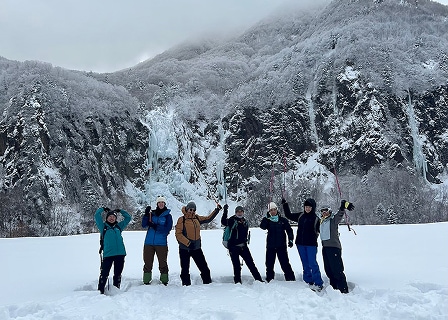 かつての鉱山跡の見晴台で不動滝をバックに記念撮影するスノーシューハイキングツアーの参加者