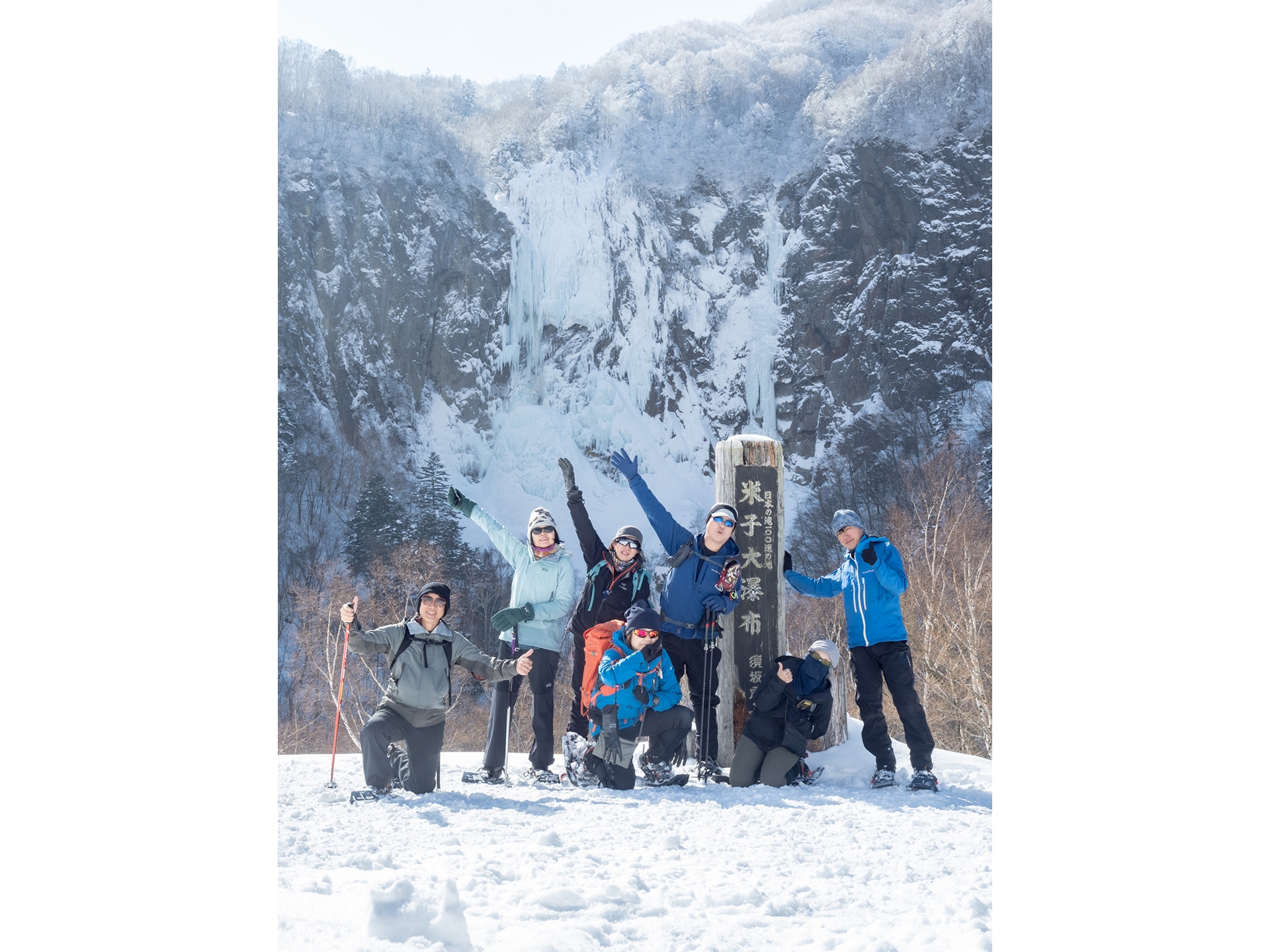 米子大瀑布の案内標の前で記念撮影するスノーシューハイキングツアーの参加者